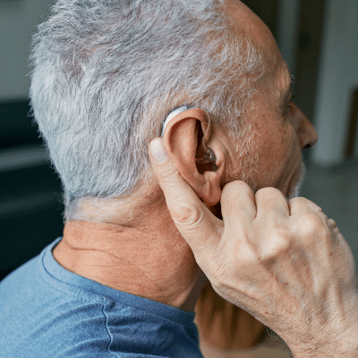 Older man showing hearing device on his ear, representing hearing protection devices