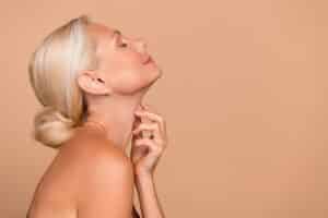 Profile of senior woman applying lotion to neck after shower, skincare concept highlighting neck lift and anti-aging treatment.