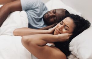 Woman frustrated by snoring partner in bed, showing sleep apnea and nighttime breathing problems at home.