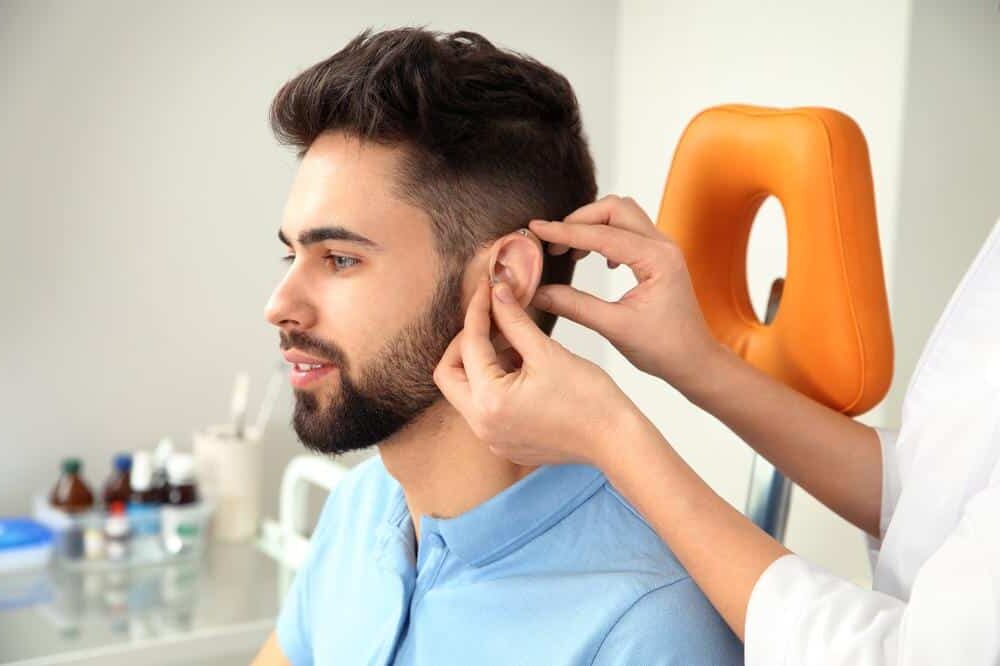 1760111156_young-man-getting-hearing-aid-checked-doctor-e1668717310270