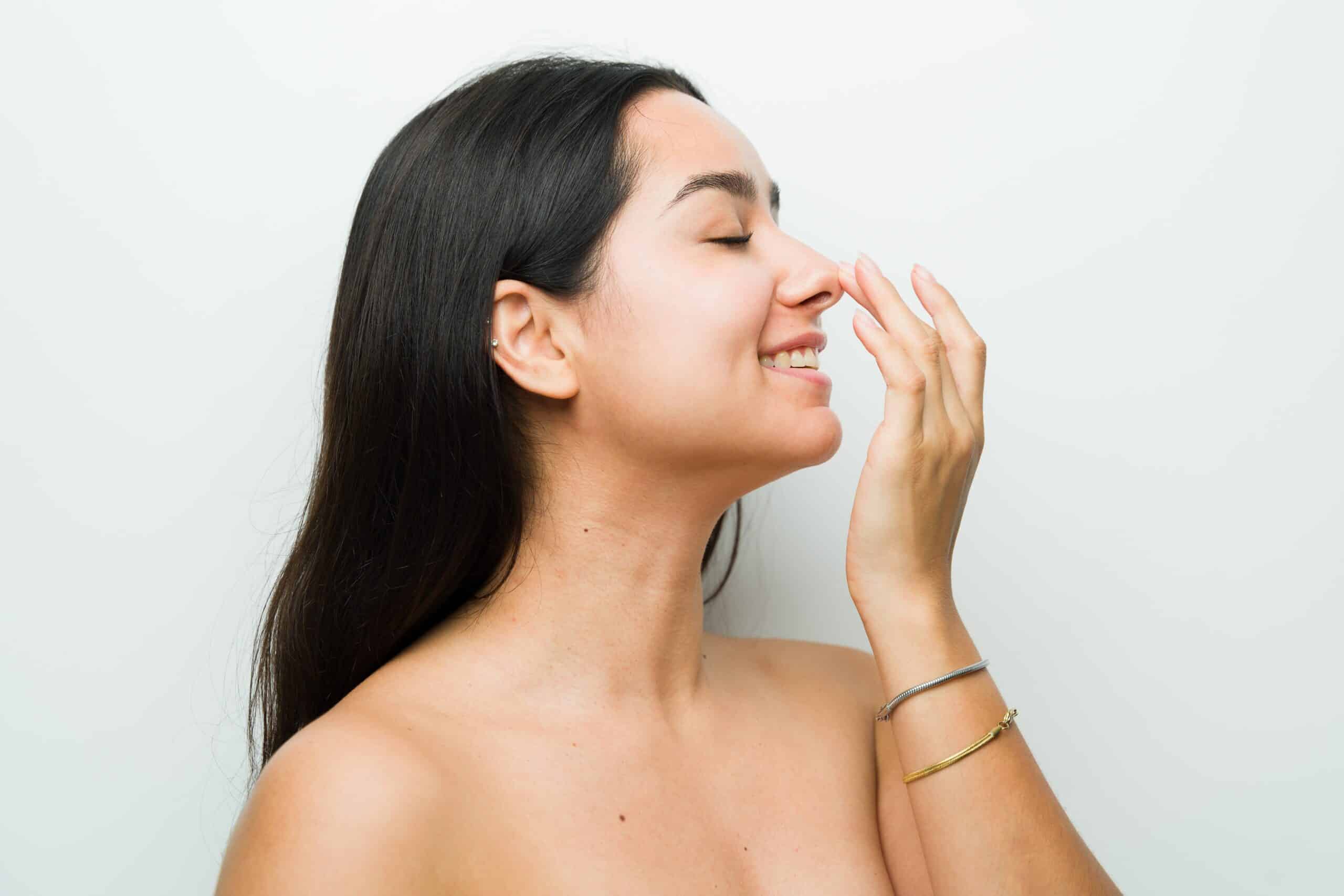 Beautiful woman touching her nose and smiling after rhinomodelation treatment, looking happy and relaxed in studio setting