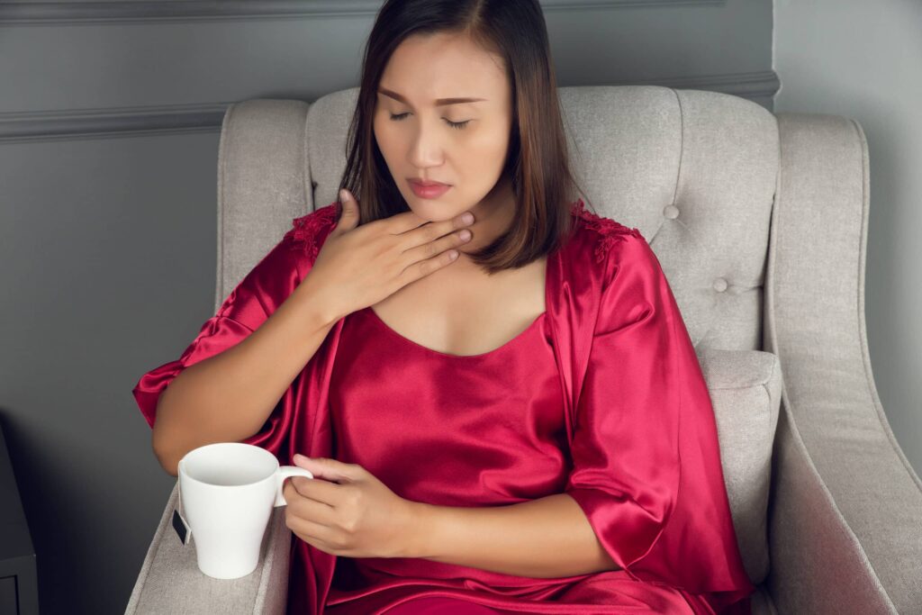 Woman touching her throat with discomfort, showing hoarseness and sore throat symptoms.