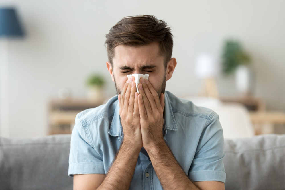 Man blowing his nose with chronic congestion symptoms at home