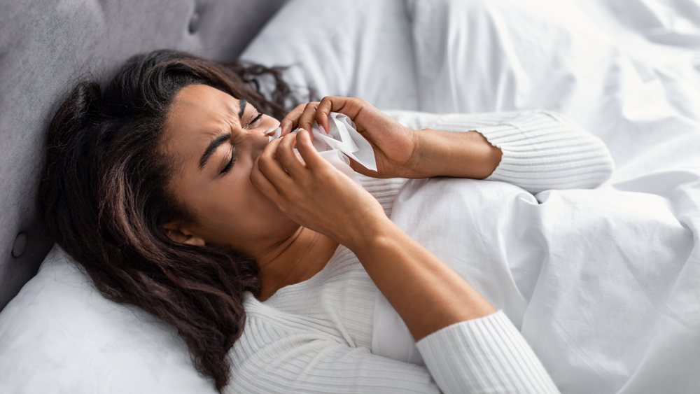 Woman blowing her nose while resting in bed with allergy or sinus infection symptoms