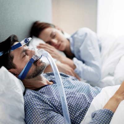 Man wearing sleep apnea device in bed beside his wife, representing sleep apnea treatment
