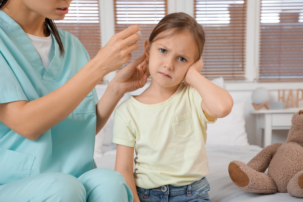 Child holding their ear while an ENT specialist examines it during an evaluation for recurring ear infections.